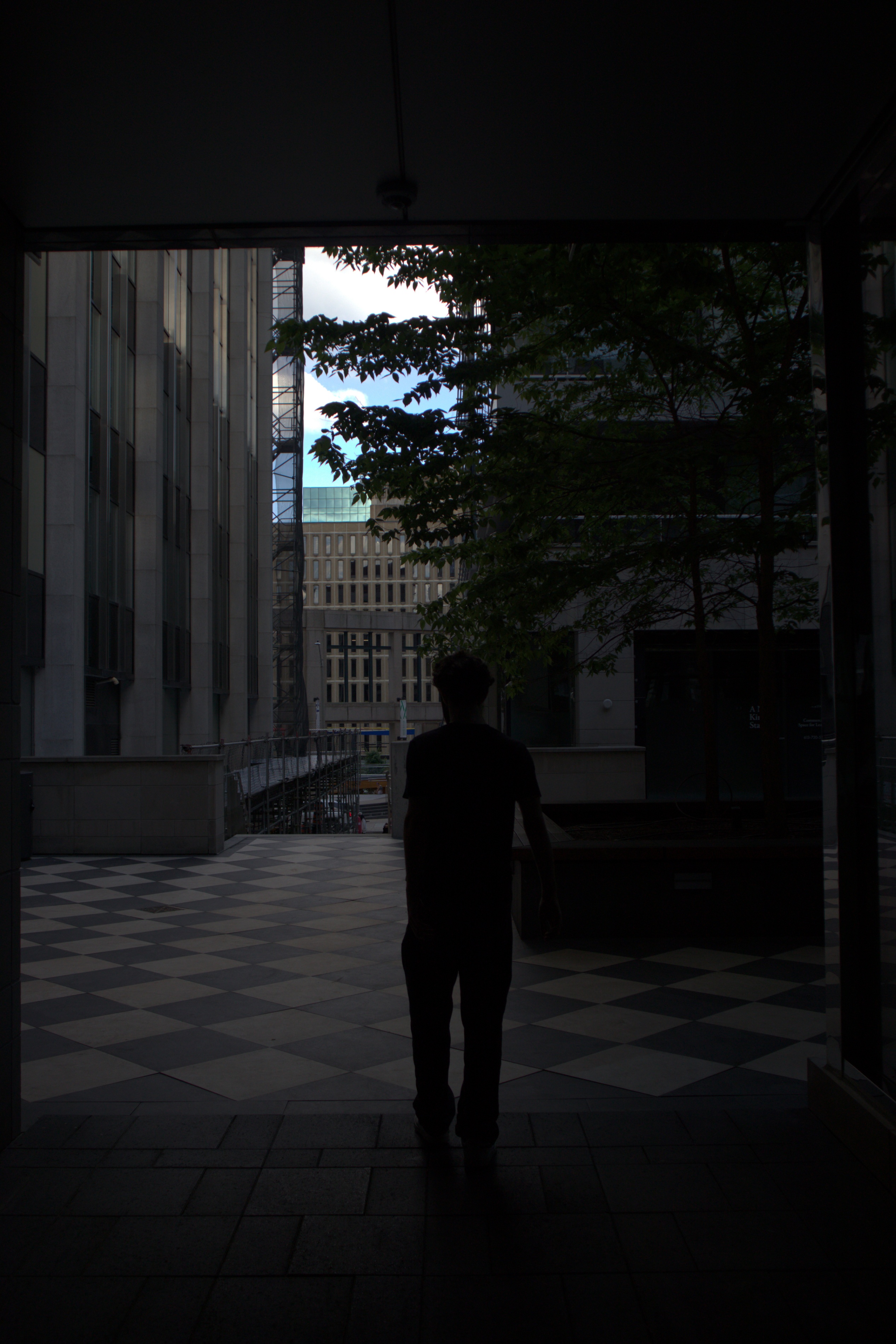 Niko Couture walking through a doorway into a checkered courtyard, framed in shadow